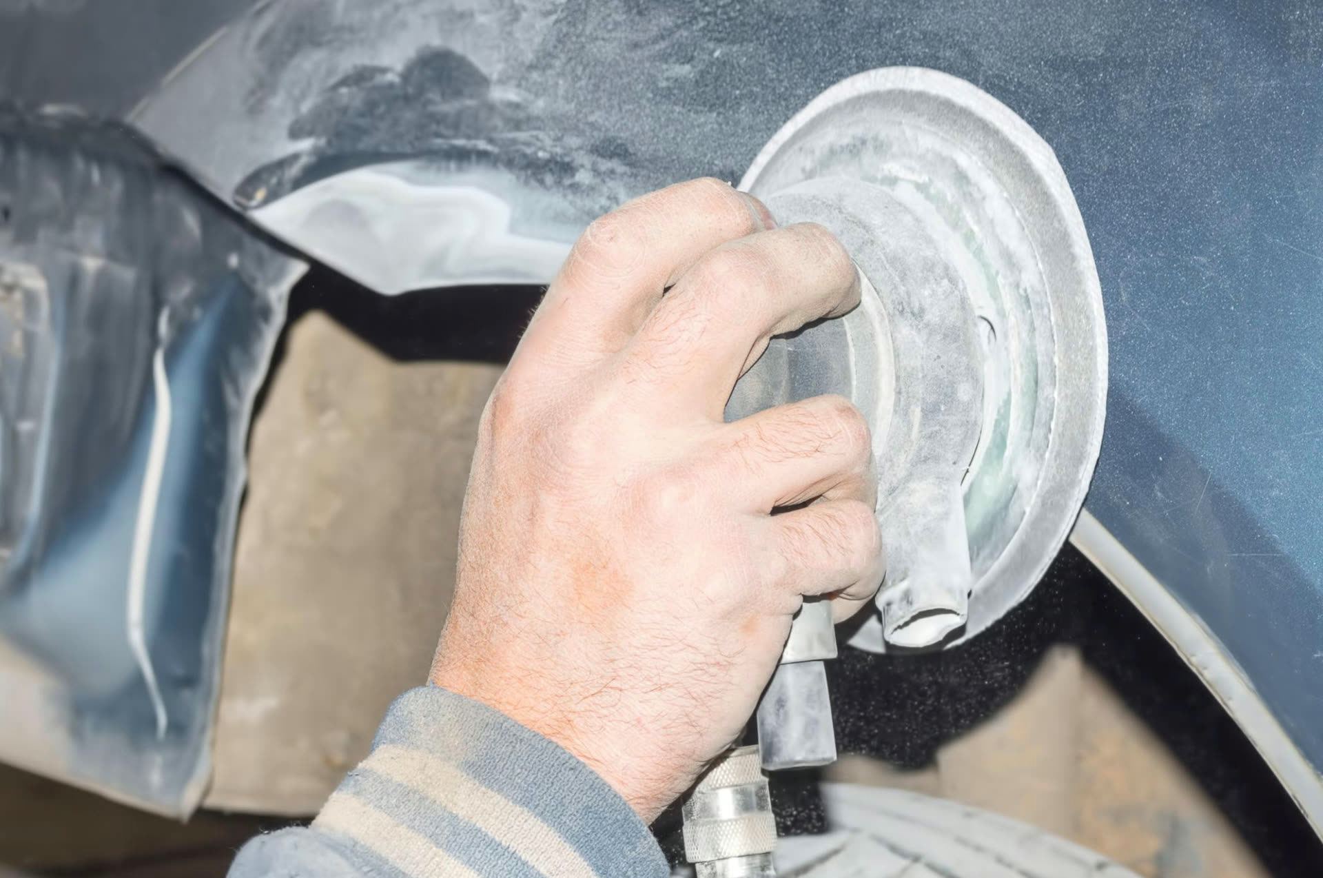 Technician's hands sanding a damaged car panel with a rotary sander