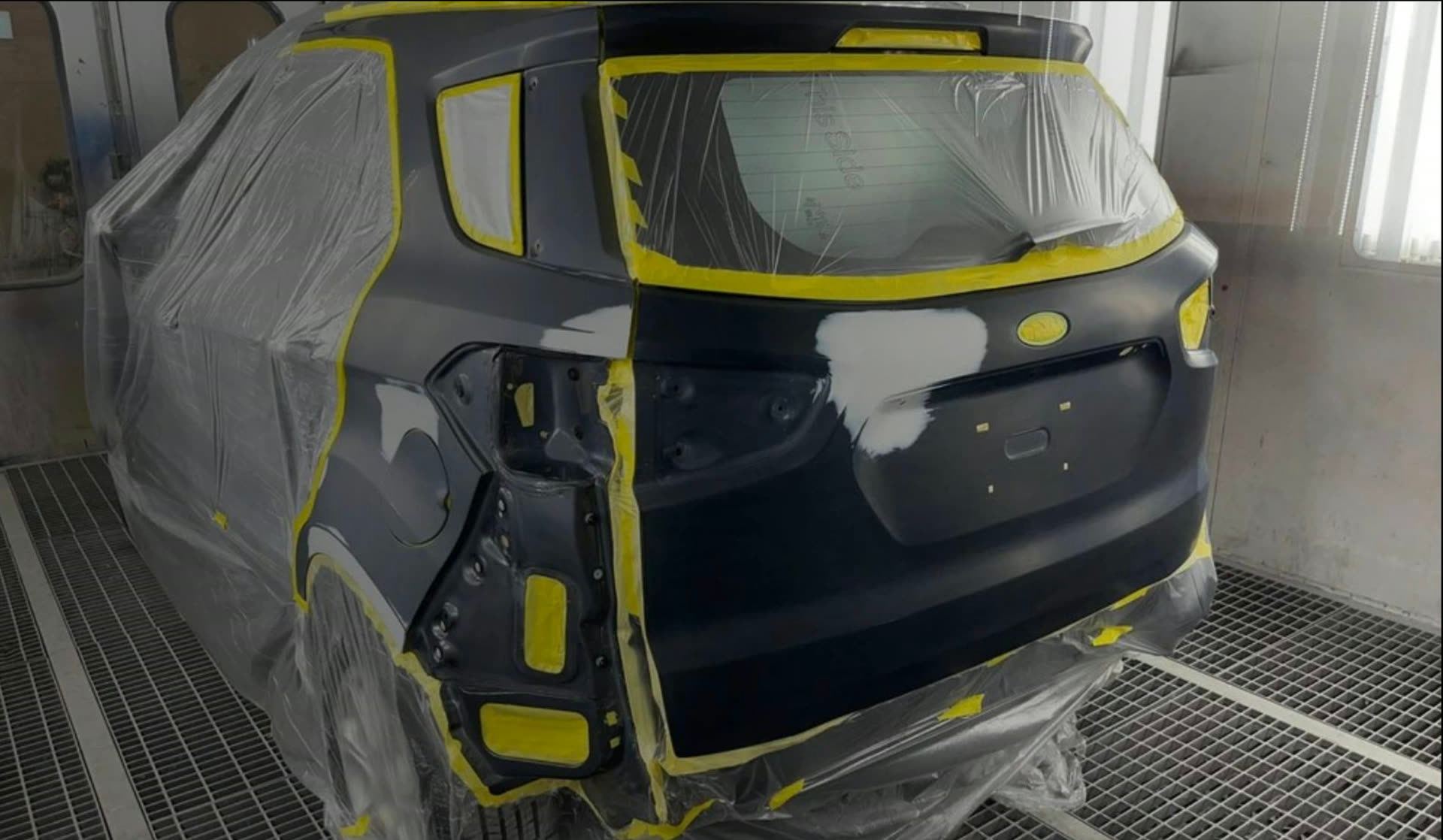 SUV with masking tape and protective sheeting in the paint booth, prepared for refinishing after collision repair