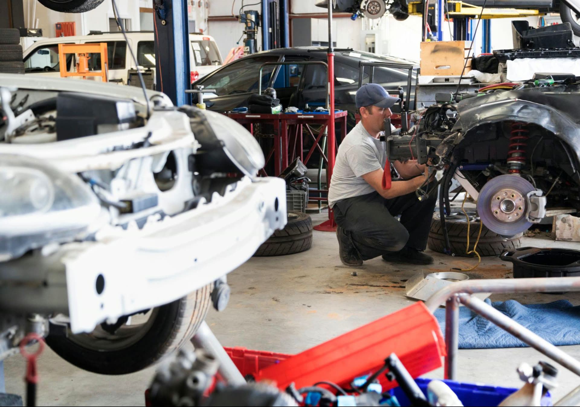 Technician working in the body shop with multiple vehicles in repair behind him